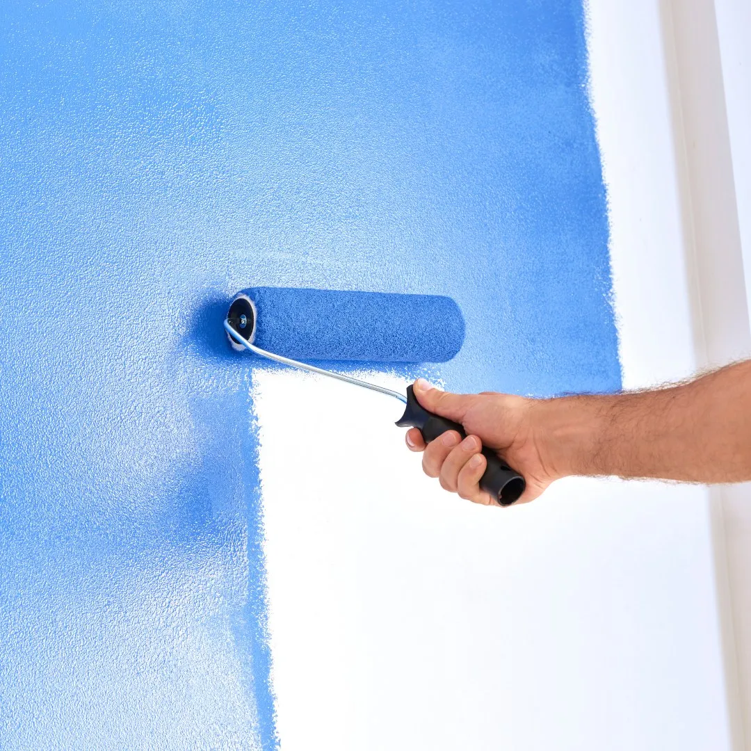 Paint roller applying blue paint to a white wall